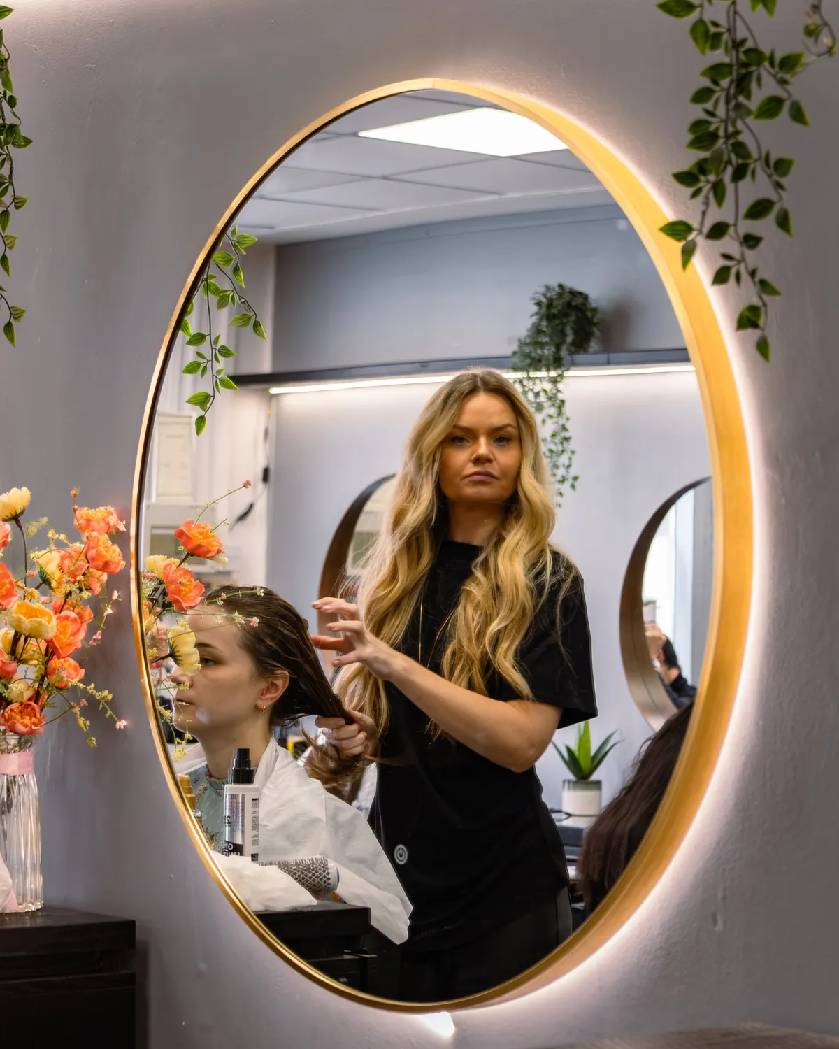 Hairdresser working with a client, reflected in a round salon mirror.