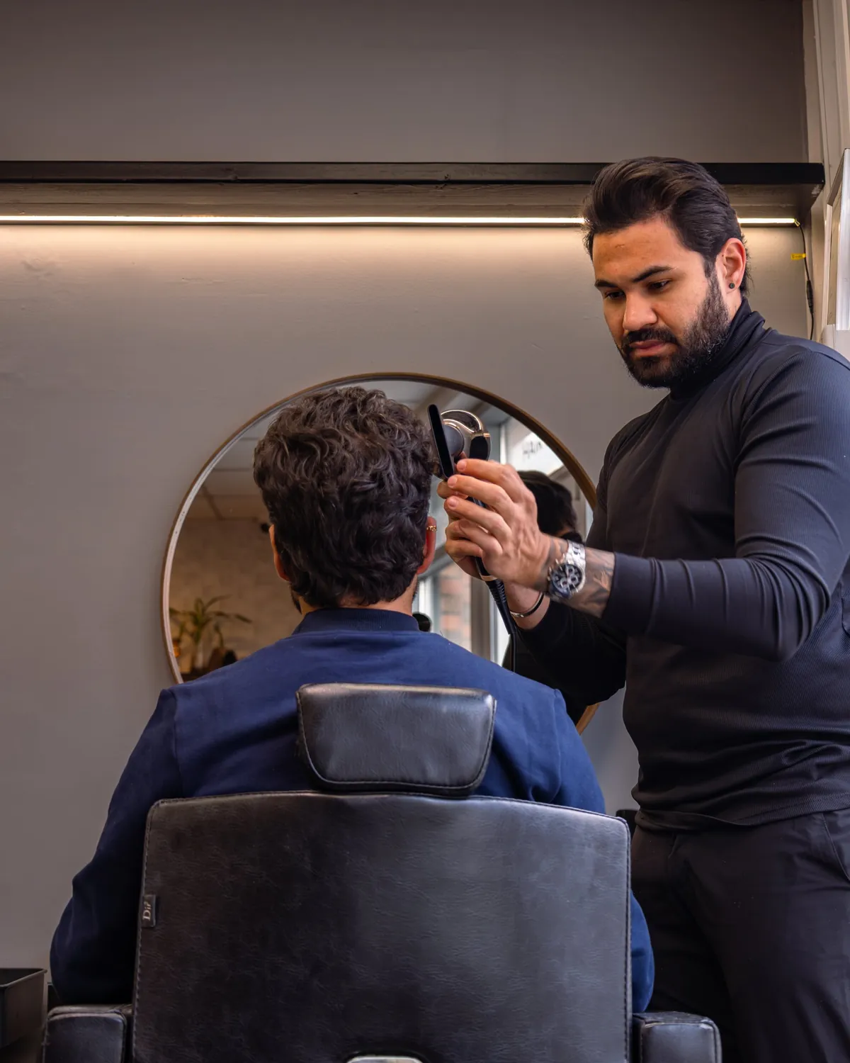 Stylist using clippers and a comb on a male client's curly hair.