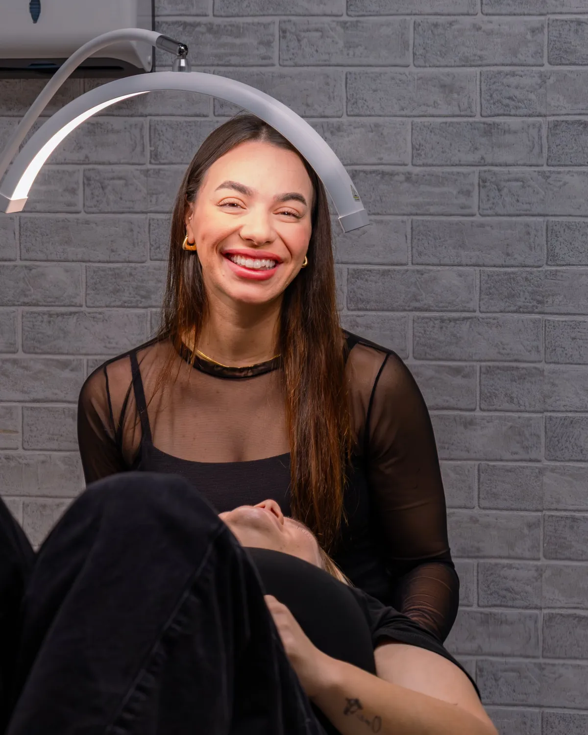 Beauty therapist smiling beneath a salon ring light.